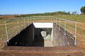 Entrada subterrânea do monumento anti-bandeirante, com corrimão metálico e uma escultura em pedra visível no interior.